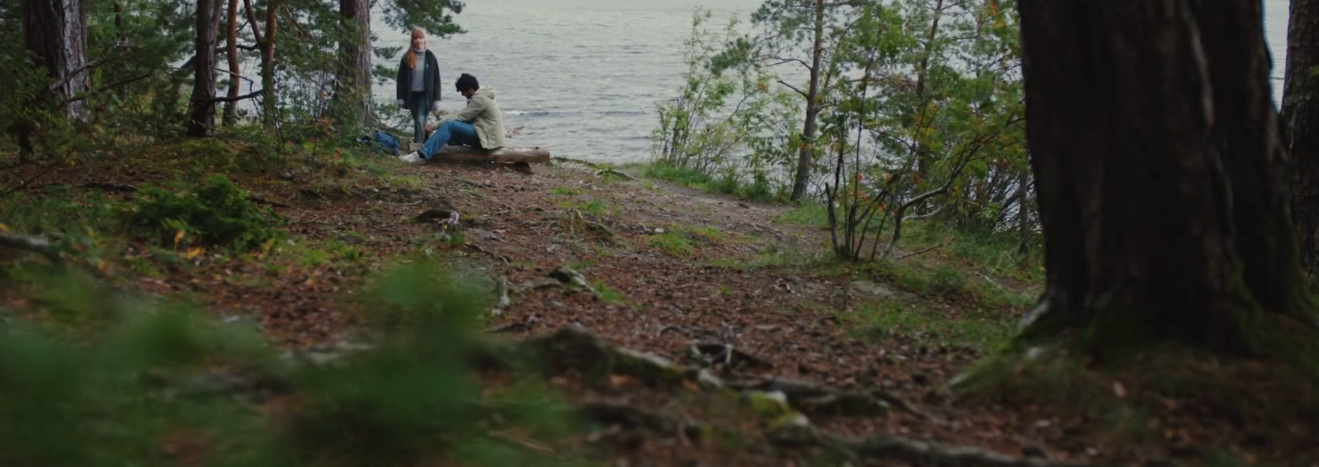 Personer sitter ved en innsjø omgitt av skog. Foto.