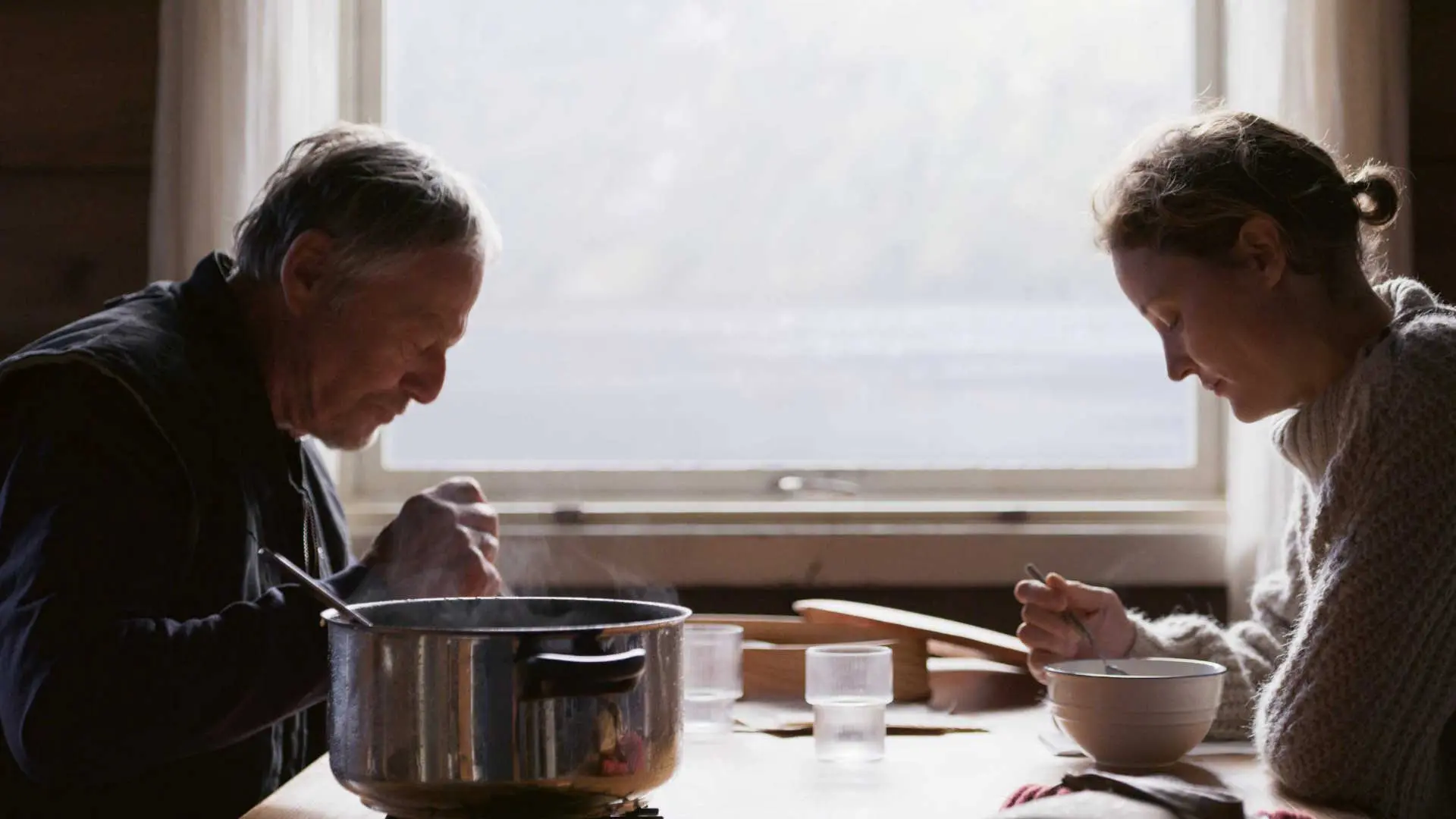 Stillbilde fra "HELENE & MATHIEU". En kvinne og en eldre mann spiser suppe. Foto.