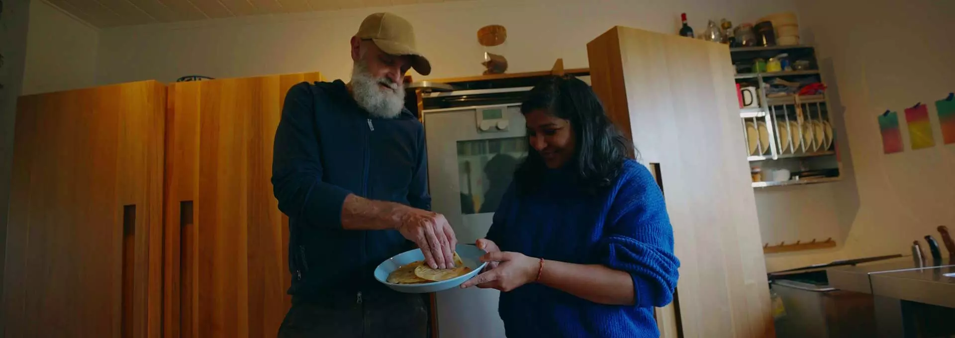 En mann og en kvinne står på et kjøkken. De ser glade ut. De smaker på en pakistansk lefse.