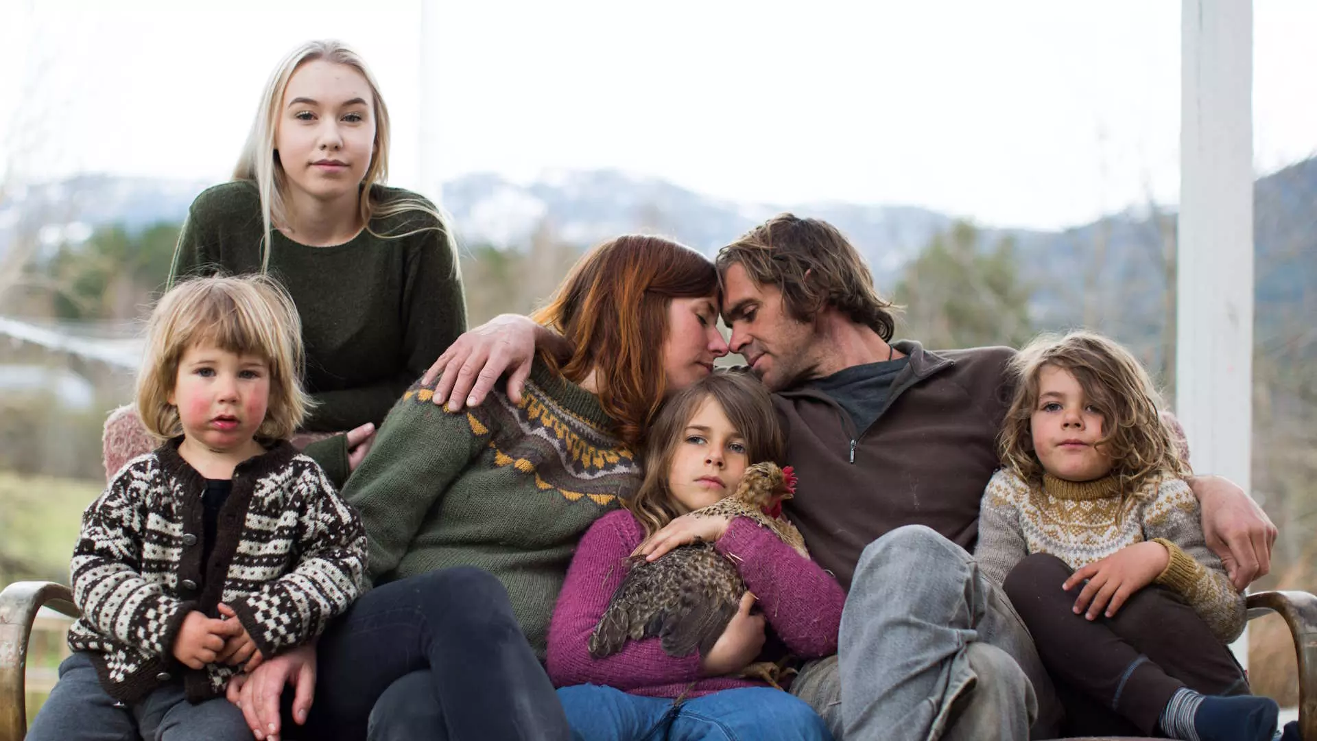 En familie på seks sitter tett sammen på en sofa utendørs, og gir en følelse av kjærlighet og samhold.