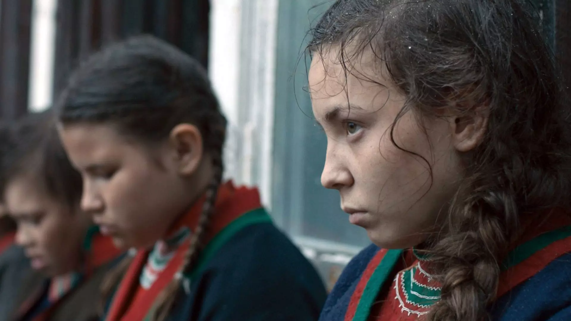 Nærbilde av noen samiske barn og ungdommer som står på en rekke. De ser triste og alvorlige ut, og har på seg kofte. 