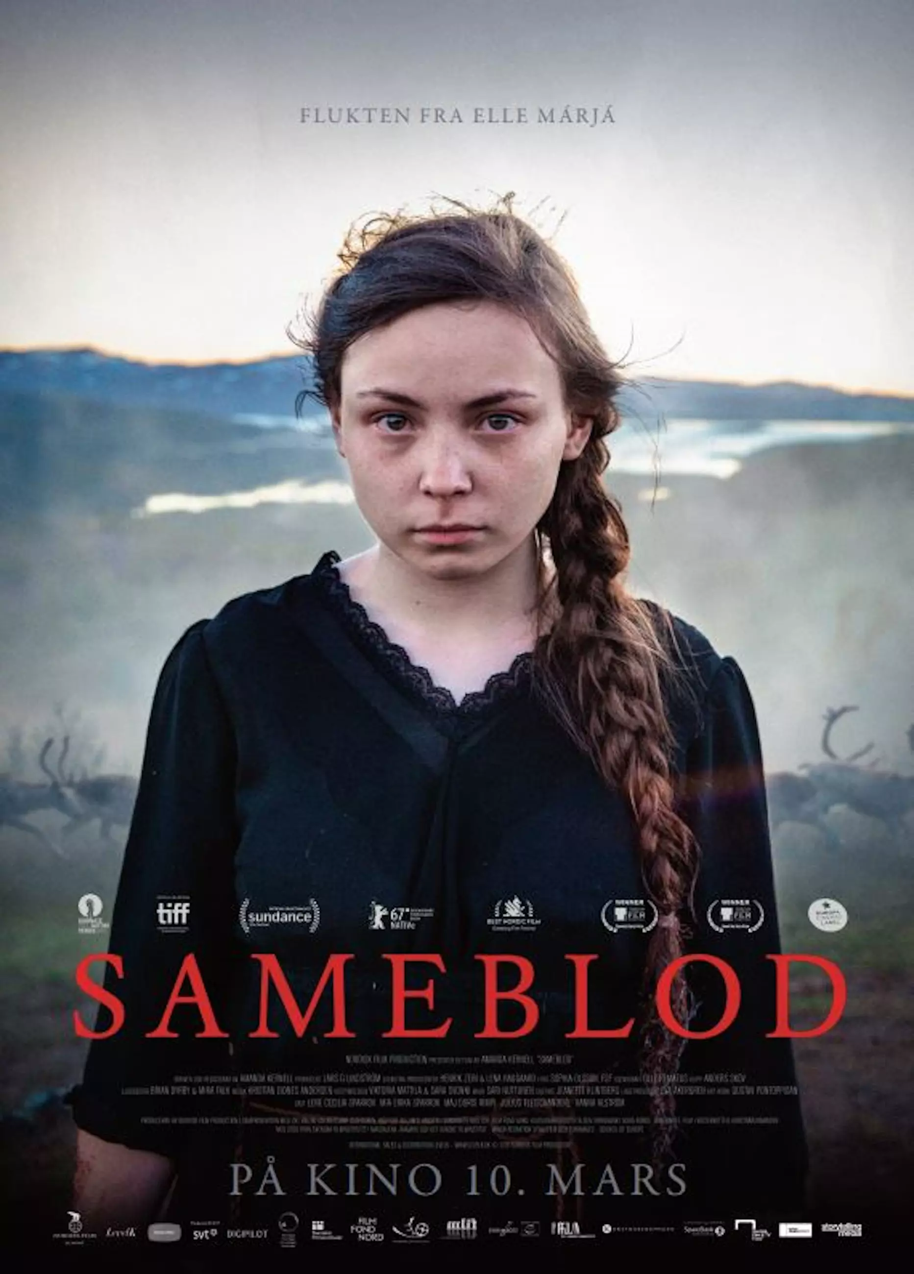 Filmplakat i stående format. Ei jente i tenårene står og ser alvorlig inn i kameraet. Hun har på seg en sort kjole og har håret i en lang flette. Bak henne skimter man nordiske fjell og reinsdyr. Tittelen “SAMEBLOD” står nederst på plakaten i store, røde bokstaver. Øverst står en liten tekst som lyder “FLUKTEN FRA ELLA MARJA”