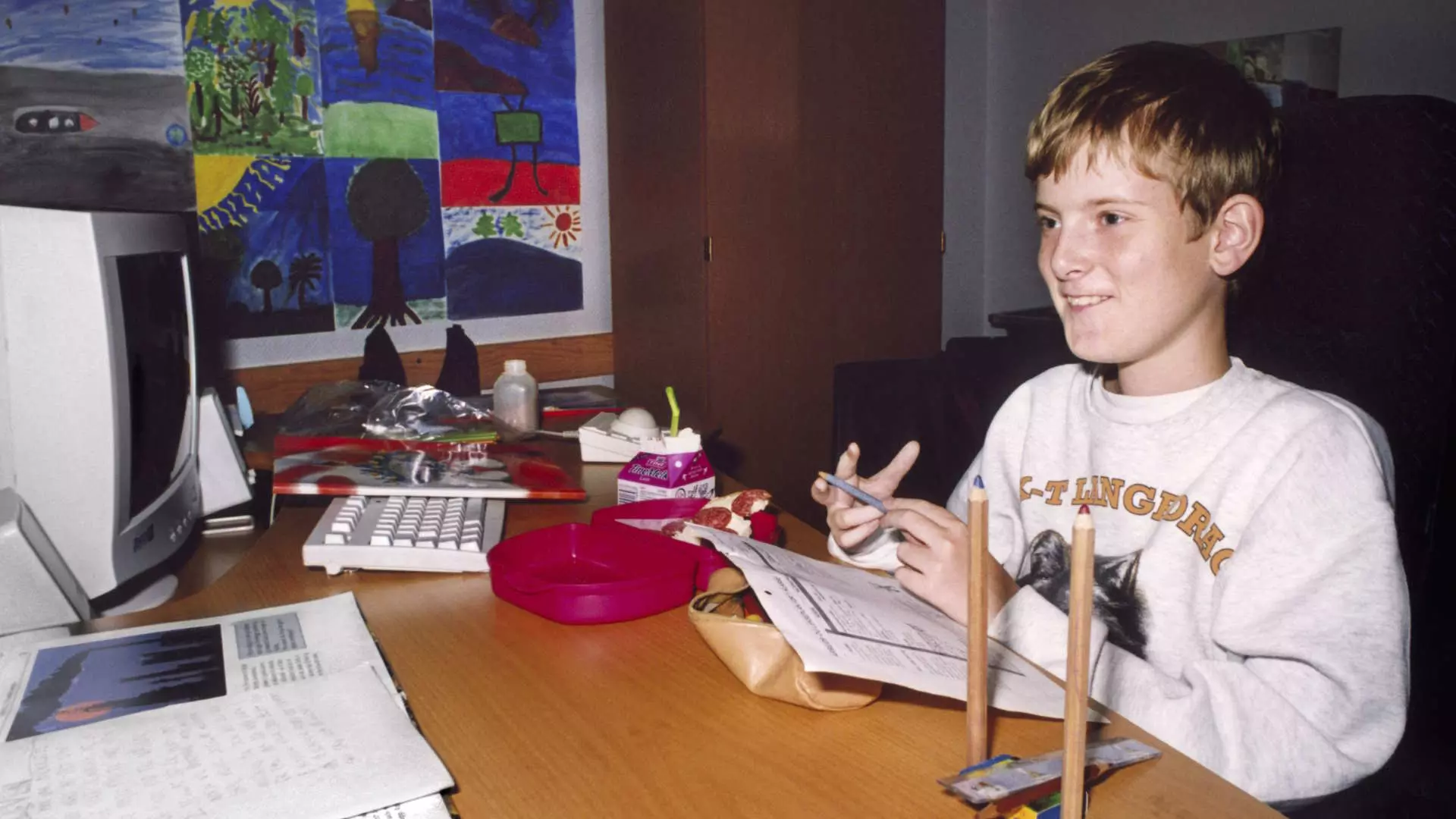 En ung gutt sitter ved et skrivebord. Det ser ut som at han muligens gjør lekser. Bildet bærer preg av at det ble tatt på tidlig 2000-tallet når det kommer til klær og interiør. Gutten smiler og har på seg en hvit genser. Vi skimter utdatert datautstyr.