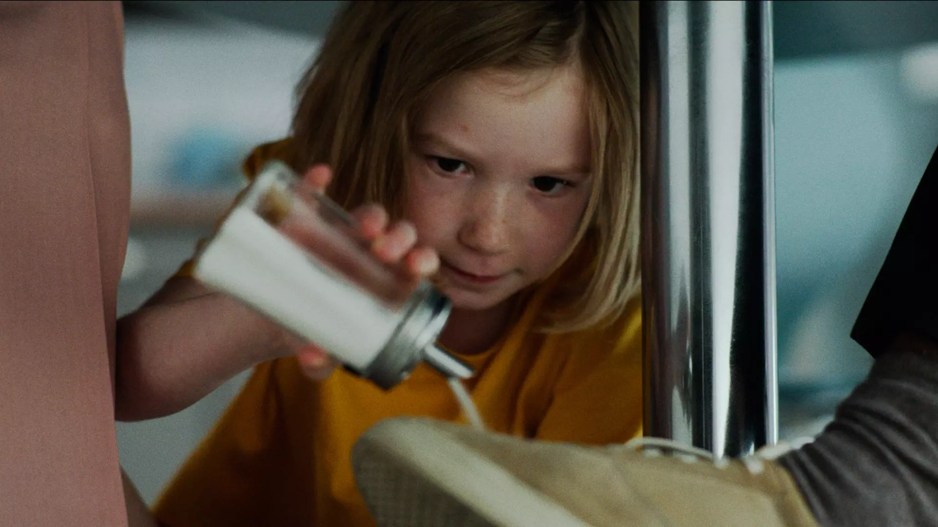 Nærbilde av en ung jente i gul t-skjorte som heller sukker på noen sko under et bord. Det ser ut som hun gjør en rampestrek. 
