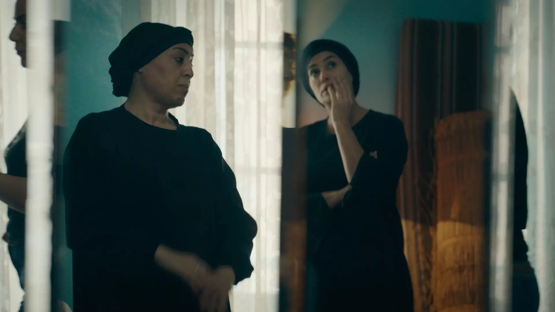 To eldre kvinner med sorte kjoler og hodeplagg ser alvorlige ut. 