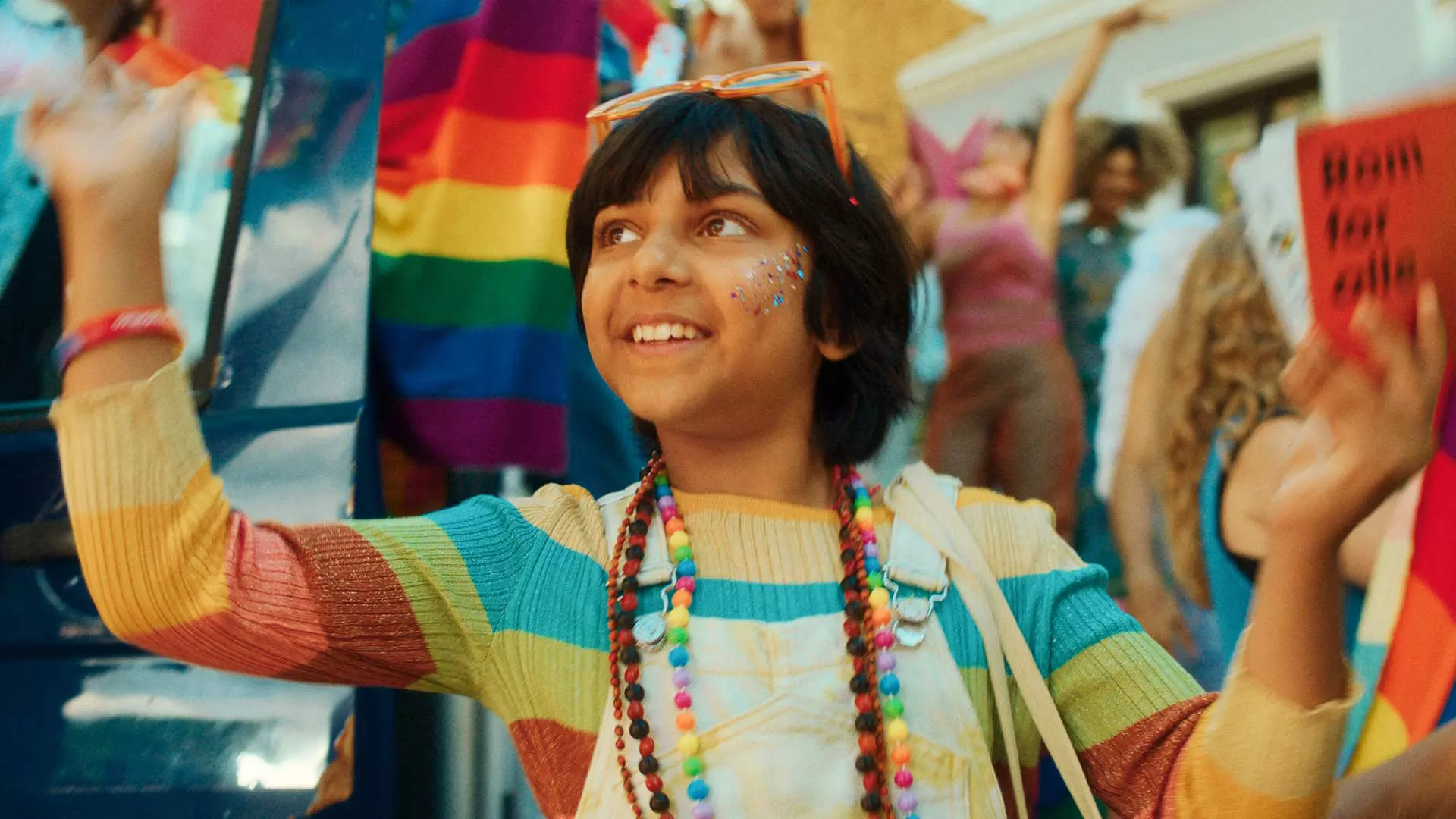 Halvnært bilde av 9 år gammel pakistansk gutt som er født i feil kropp som går i pride-parade. Feststemning. Regnbueflagg.
