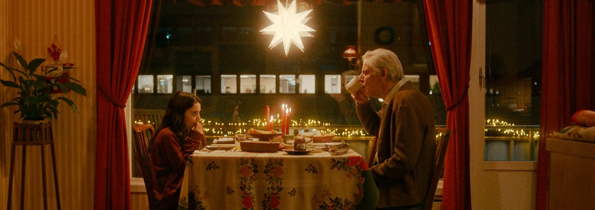 Stillbilde fra "Stargate - en julefortelling". En jente og en eldre mann spiser julemat ved et koselig bord. Foto.
